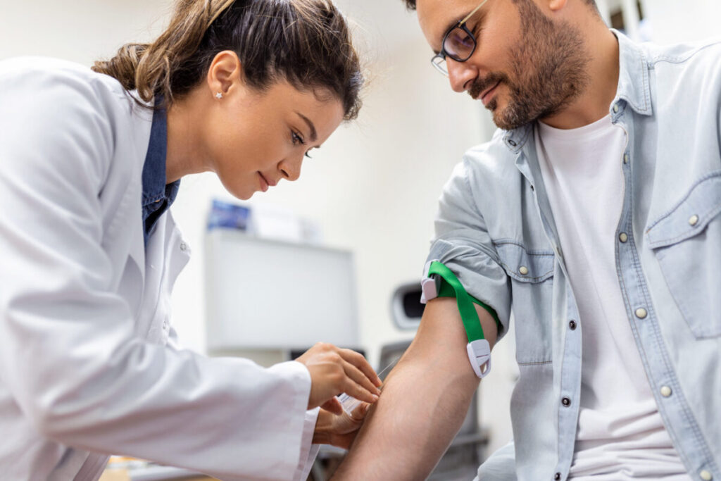 Friendly hospital phlebotomist collecting blood sample from patient in lab. Preparation for blood test by female doctor medical uniform on the table in white bright room Vrouwelijke arts neemt bloed af bij mannelijke patient.