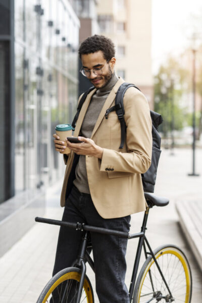 young-adult-cycling-work-city-600x900-1-400x600 Mannelijke professional met fiets op weg naar het werk checkt onderweg zijn telefoon.